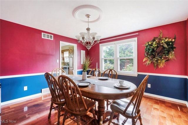 dining space featuring visible vents, light wood finished floors, baseboards, and an inviting chandelier