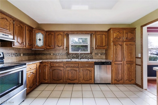 kitchen featuring decorative backsplash, appliances with stainless steel finishes, brown cabinets, a sink, and under cabinet range hood
