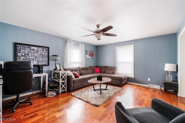 living area featuring a textured ceiling, a ceiling fan, baseboards, wood finished floors, and visible vents