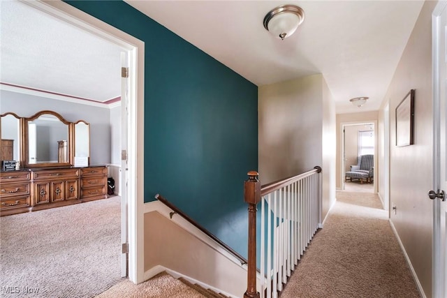 hall featuring carpet flooring, baseboards, and an upstairs landing