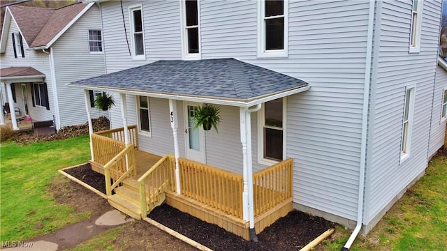 property entrance featuring a porch, a yard, and roof with shingles