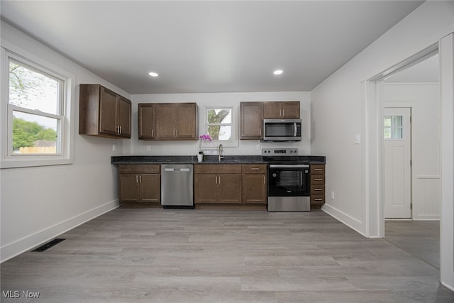 kitchen with appliances with stainless steel finishes, dark countertops, a sink, light wood-style floors, and recessed lighting