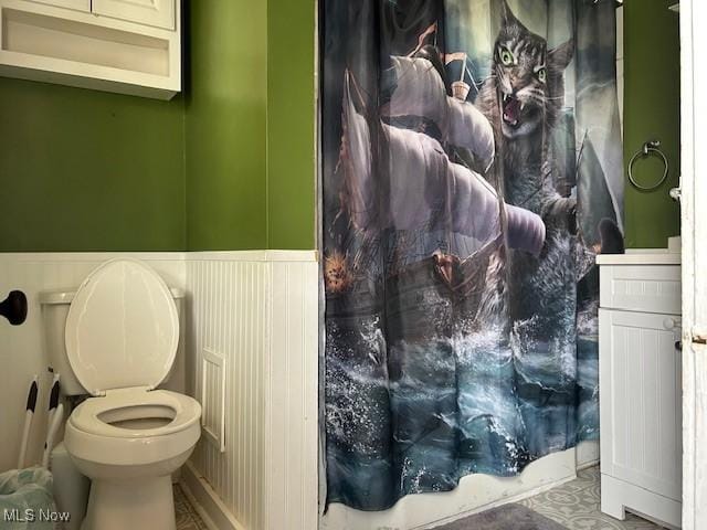 bathroom with a wainscoted wall, a shower with shower curtain, and toilet