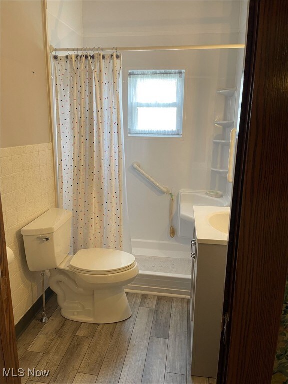23314 Frostyville Rd, Caldwell, OH 43724 - full bathroom featuring toilet, a shower stall, wood finished floors, wainscoting, and tile walls