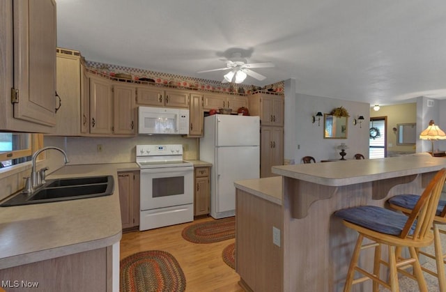 kitchen featuring light countertops, light wood finished floors, white appliances, a kitchen bar, and a sink