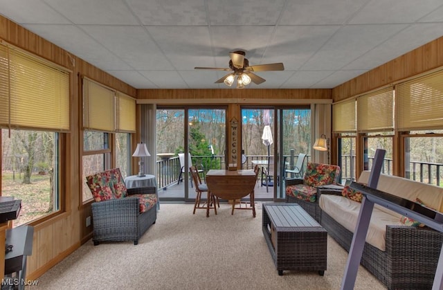 sunroom featuring carpet flooring, a ceiling fan, a drop ceiling, and wooden walls