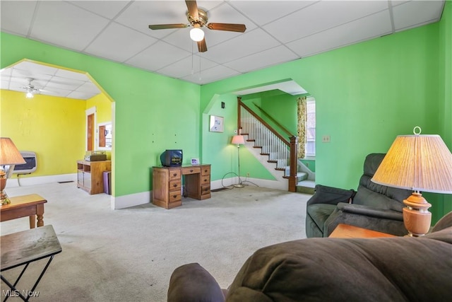 living area with arched walkways, ceiling fan, and a drop ceiling