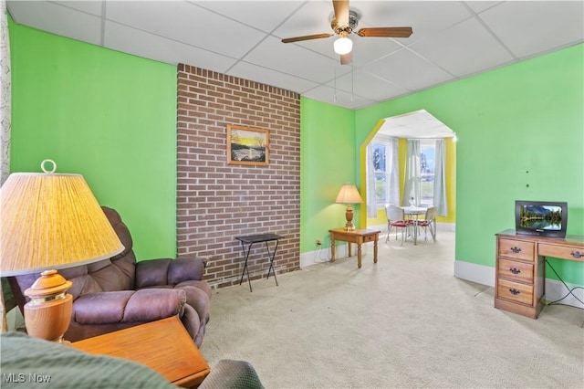 living area with baseboards, a drop ceiling, carpet floors, arched walkways, and ceiling fan