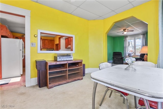 carpeted dining space with a paneled ceiling, baseboards, and ceiling fan