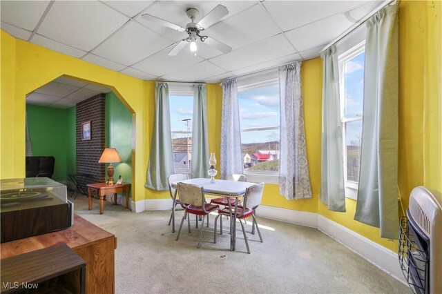 carpeted dining area featuring heating unit, baseboards, ceiling fan, and a drop ceiling