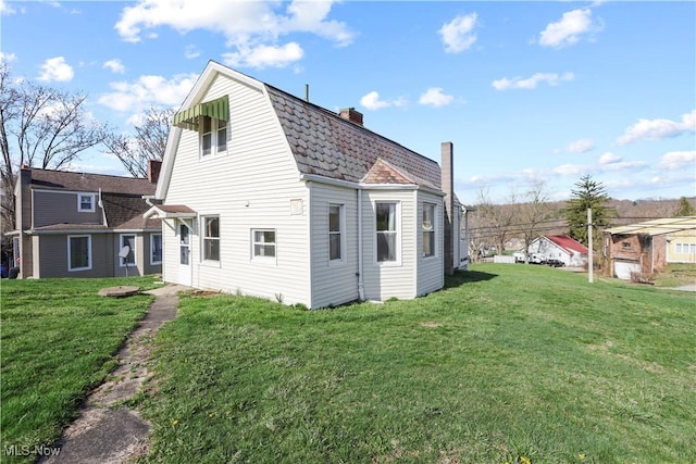 back of property with a gambrel roof, a chimney, and a lawn