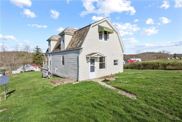 rear view of property with central air condition unit, a gambrel roof, and a yard
