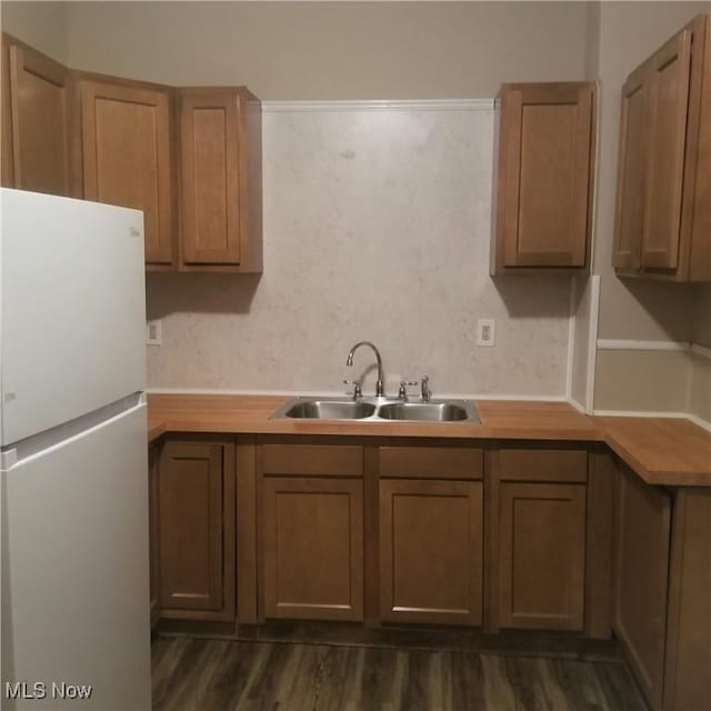 kitchen featuring freestanding refrigerator, dark wood-style flooring, light countertops, a sink, and brown cabinets