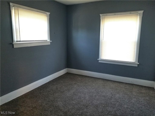 spare room with dark carpet, a healthy amount of sunlight, and baseboards