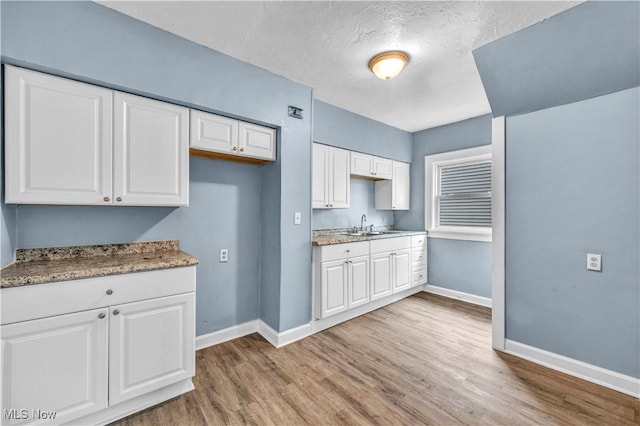 kitchen with baseboards, white cabinetry, and light wood-style flooring