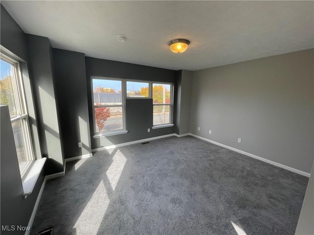 empty room featuring dark colored carpet, visible vents, and baseboards