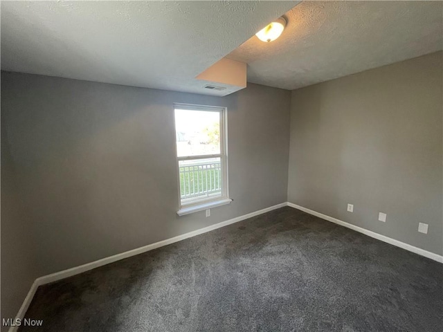 unfurnished room with dark carpet, baseboards, visible vents, and a textured ceiling