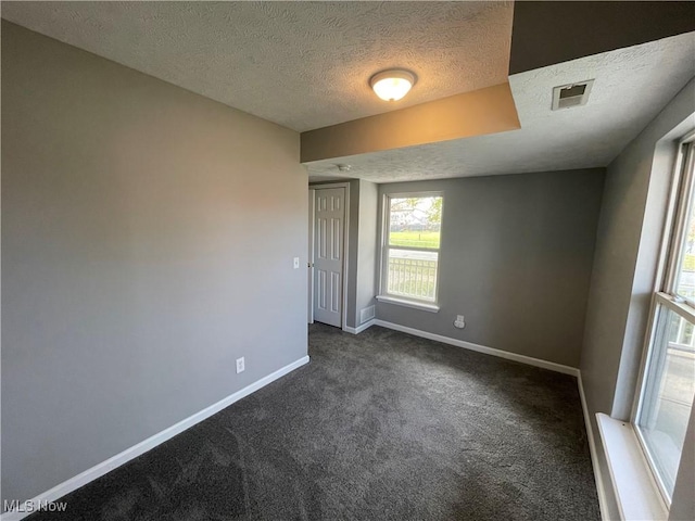 empty room with dark carpet, baseboards, visible vents, and a textured ceiling