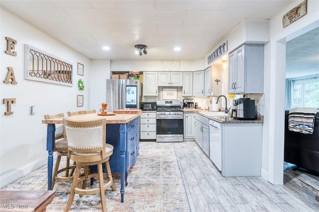 kitchen featuring stainless steel appliances, wood tiled floor, a sink, a breakfast bar area, and backsplash