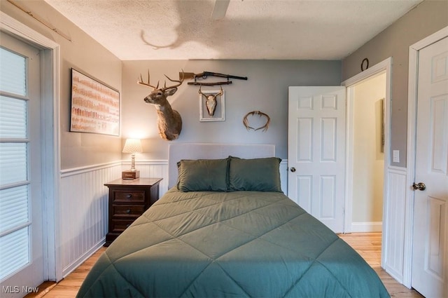 bedroom with a textured ceiling, light wood-type flooring, and wainscoting