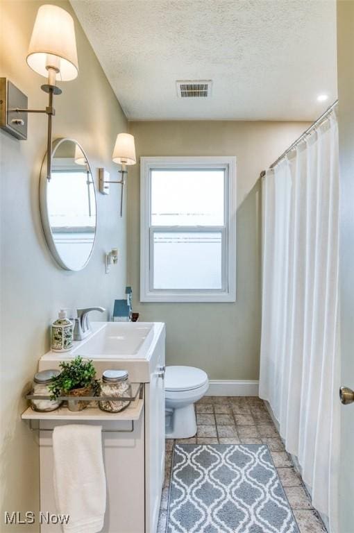 bathroom with vanity, toilet, baseboards, a textured ceiling, and visible vents