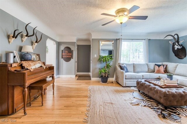 living area with baseboards, a textured ceiling, a ceiling fan, and light wood finished floors