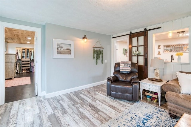 living area with baseboards, a barn door, a textured ceiling, and wood finished floors