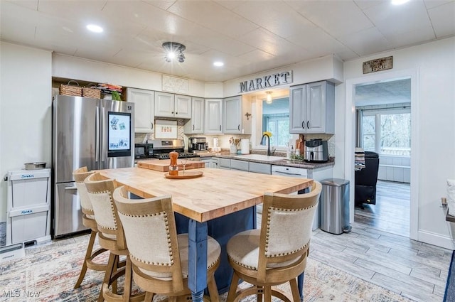 kitchen featuring butcher block counters, appliances with stainless steel finishes, a sink, gray cabinets, and a kitchen breakfast bar