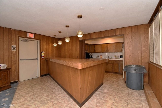 3333 Warrensville Center Rd Unit 204, Shaker Heights, OH 44122 - kitchen with light countertops, wood walls, a peninsula, brown cabinets, and hanging light fixtures