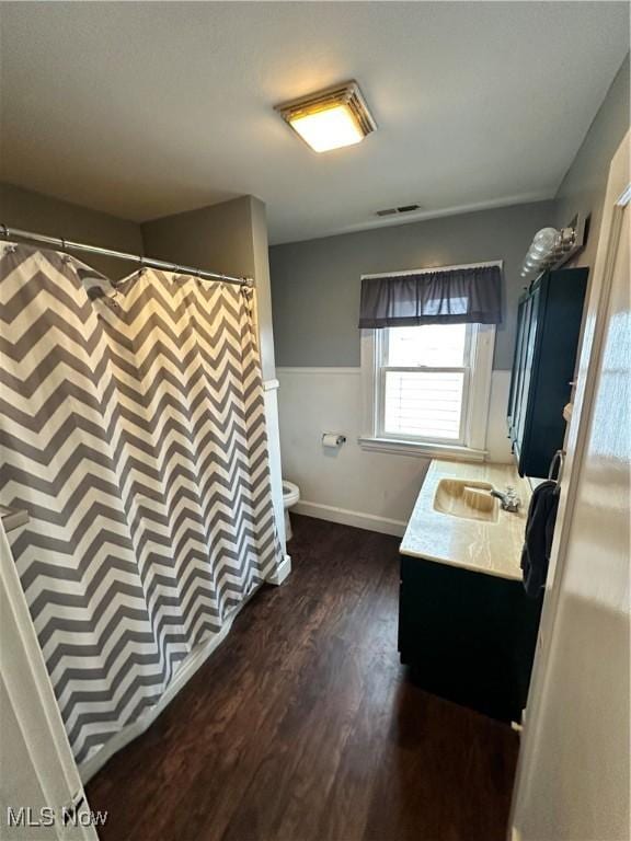 full bath with toilet, vanity, wood finished floors, wainscoting, and visible vents