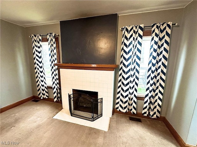 carpeted living area with a tile fireplace, baseboards, and visible vents
