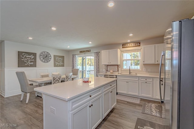 kitchen featuring freestanding refrigerator, light wood-style flooring, white cabinets, a sink, and wainscoting