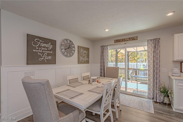 dining area with wood finished floors, a decorative wall, and a wainscoted wall