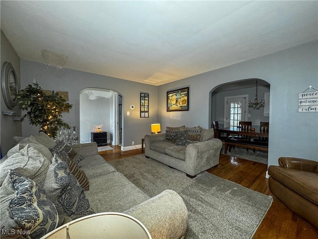 living room with arched walkways, a notable chandelier, baseboards, and wood finished floors