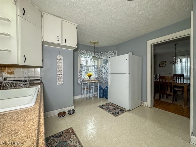 kitchen with white cabinets, an inviting chandelier, a sink, freestanding refrigerator, and light floors