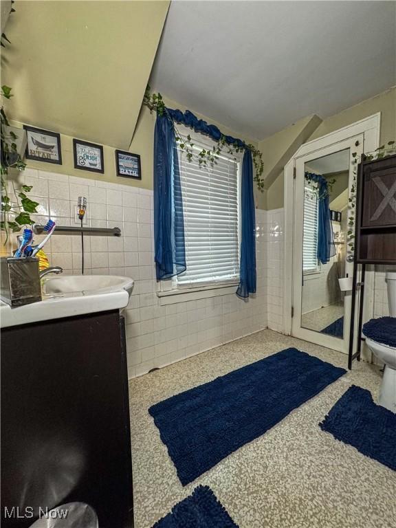 bathroom with vanity, walk in shower, toilet, a wainscoted wall, and tile walls