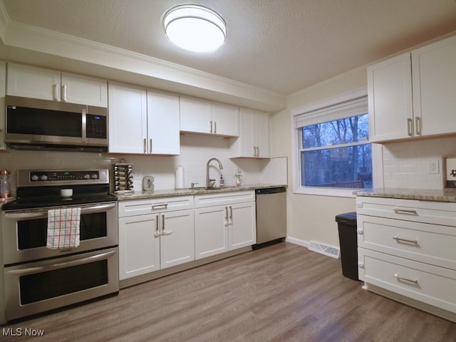 kitchen featuring ornamental molding, white cabinetry, light wood-style floors, stainless steel appliances, and a sink