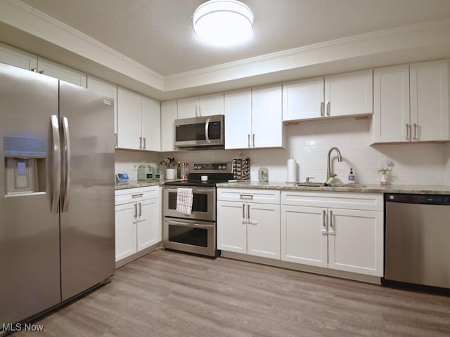 kitchen with light wood-style flooring, white cabinetry, appliances with stainless steel finishes, light stone counters, and a sink