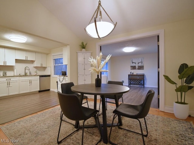 dining room featuring baseboards, light wood finished floors, and lofted ceiling