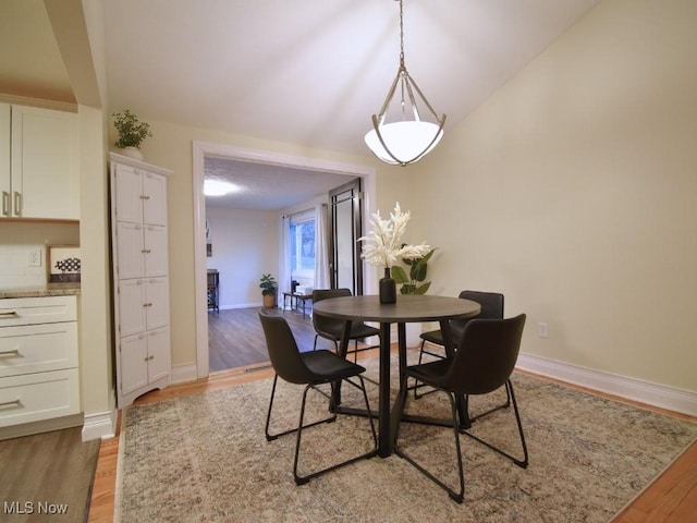 dining space featuring light wood-style flooring, baseboards, and lofted ceiling