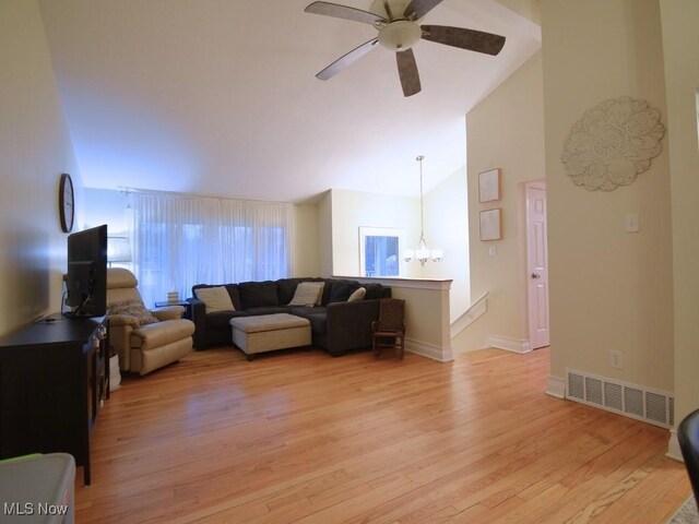 living area featuring ceiling fan with notable chandelier, high vaulted ceiling, light wood-type flooring, visible vents, and baseboards