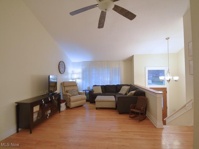 living room featuring baseboards, light wood-type flooring, vaulted ceiling, and ceiling fan with notable chandelier