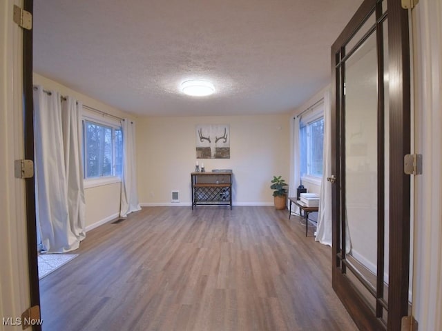 unfurnished living room featuring visible vents, baseboards, wood finished floors, and a textured ceiling