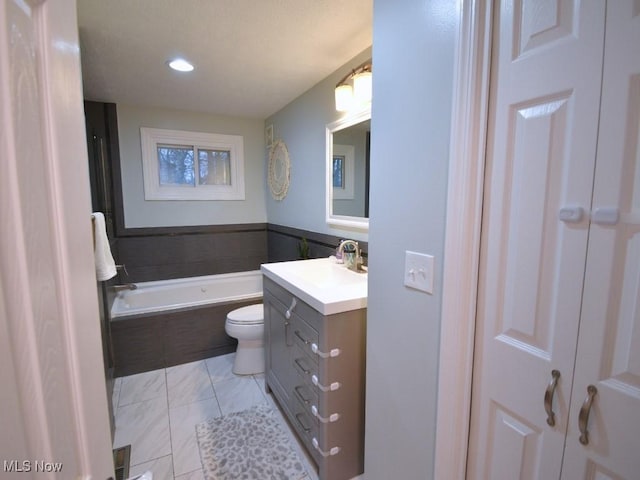 full bath featuring vanity, recessed lighting, toilet, a bath, and wainscoting