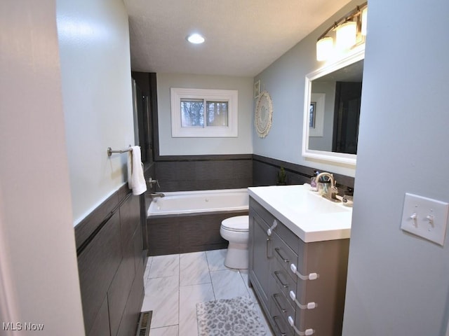 bathroom featuring toilet, vanity, tiled bath, and a wainscoted wall