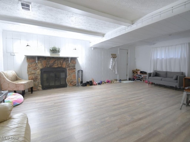 living room featuring beam ceiling, a stone fireplace, wood finished floors, and a textured ceiling
