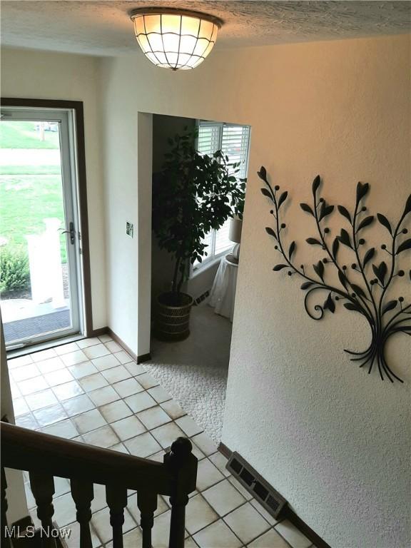 entryway featuring visible vents, light tile patterned flooring, a textured wall, and a textured ceiling