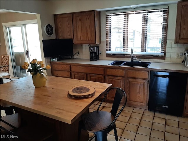 kitchen featuring tasteful backsplash, light tile patterned floors, black dishwasher, a sink, and wooden counters