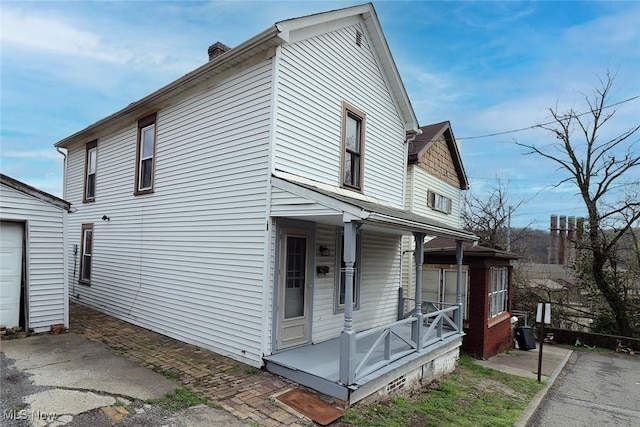 view of home's exterior with a chimney, covered porch, and a garage