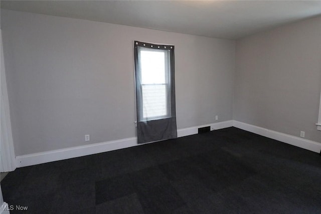 unfurnished room with dark carpet and baseboards